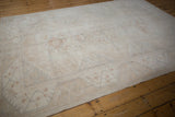 Distressed vintage Oushak rug side with ivory, beige, silver tones and scrolling border.