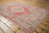 Distressed Oushak rug corner showcasing pale red, powder blue geometric pinwheel motifs and worn texture.