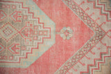 Geometric floral motifs and distressed pile on vintage Oushak rug, featuring blush pink, beige, powder blue.