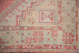 Distressed Oushak rug corner, geometric patterns in faded red, ivory, with visible wear.