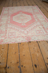 Distressed Oushak rug corner with pale red, ivory, and blue geometric pinwheels.