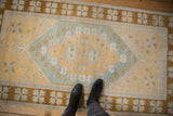 Distressed Oushak rug featuring saffron yellow field, dusty blue floral motifs, bronze border.
