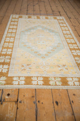 Vintage distressed Oushak rug: end fringe, wide bronze border, ivory quatrefoil floral motifs.