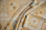 Folded vintage Oushak rug showing decorative muted saffron and blue floral patterns with distressed texture.