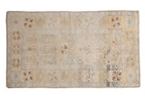Decorative distressed Oushak rug in muted ivory, saffron, and charcoal with overall subtle patterns.