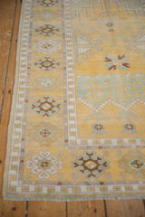 Distressed Oushak rug with saffron yellow field, geometric border, and germinating plant motif.