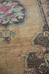 Close-up of vintage distressed Oushak rug showing worn beige pile, fuchsia and mint floral details.