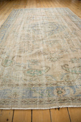 Distressed Oushak rug pile close-up: worn beige, pale blue vines, and visible knot heads.