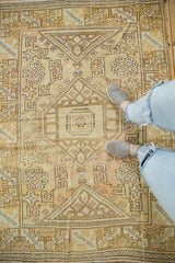 Geometric hook and latch motifs on distressed vintage Oushak rug in soft gold and pale rose.