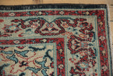Distressed Oushak rug corner, showing cherry red cloudband border, sky blue tendrils, and even wear.