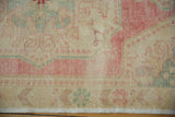 Fringed lower edge of vintage Oushak rug, showing distressed rose, seafoam, and beige floral motifs.