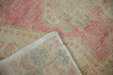 Distressed rose and beige pile texture of vintage Oushak rug, showing hand-knotted foundation and fringe.