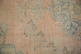 Distressed vintage Oushak pile texture with soft peach and blue-green floral design.
