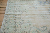 Distressed vintage Oushak rug texture with faded ivory field and soft green scrolling patterns.