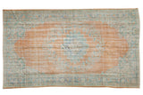 Distressed vintage Oushak rug, tangerine orange field, faded floral medallion, and pale blue-green hues.