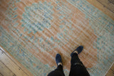 Distressed Oushak carpet texture in faded tangerine, pale blue, and ivory floral motifs.