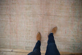 Distressed Oushak carpet's worn pile, revealing faint scrolling vinery in soft ivory and green.