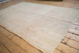 Distressed Oushak carpet with even wear, featuring faded ivory and pale green scrolling patterns.