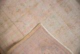 Folded corner of a distressed Oushak rug, showing worn pale pile and visible hand-knotted foundation.