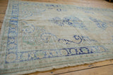 Distressed Oushak carpet corner with worn ivory pile, pale blue border, and foundation showing.