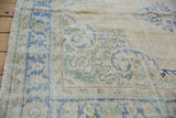Distressed Oushak rug corner with fringe, showing pale blue, seafoam green, and foundation.