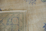 Folded vintage Oushak rug corner revealing wear, fringe, side selvage, and striped foundation.
