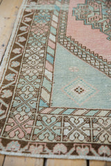 Vintage distressed Oushak rug corner showing blush, ocean green palmettes and geometric borders.