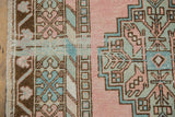 Distressed vintage Oushak rug close-up featuring blush, mint green, and bronze geometric border design.