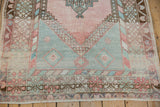 Distressed vintage Oushak rug lower corner, highlighting even wear and geometric border in blush and mint green.