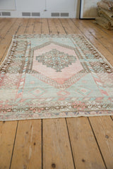 Distressed Oushak rug's pale rose and mint green delicate vine outer border.