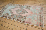 Distressed Oushak rug corner, revealing blush and mint vine border with intact selvage.