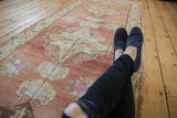 Distressed Oushak runner with abrashed pale raspberry field and scrolled ivory motifs.