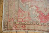 Vintage distressed Oushak rug corner, showing worn rose, slate patterns and short fringe.
