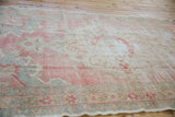Distressed Oushak rug bottom border with pale brick red, slate floral motifs, and ivory fringe.