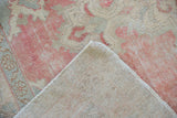 Distressed Oushak rug corner displaying faded pink pile, visible knot heads, and original selvage.