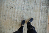 Distressed Oushak carpet texture with mostly even wear, ivory field, and faded blue floral motifs.
