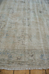 Distressed Oushak rug pile with faded ivory, beige, blue patterns, showing visible fringe.