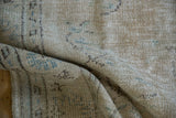 Distressed texture of vintage Oushak rug, revealing worn beige, ivory, and pale blue motifs.