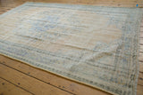 Angled view of a vintage Oushak carpet, highlighting its distressed low pile and visible foundation.