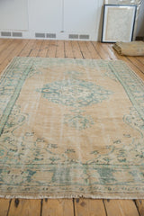 Visible cross hatch foundation and wear on a distressed beige and seafoam green Oushak rug.