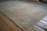 Vintage distressed Oushak rug corner, showing worn texture, side selvage, and green border.