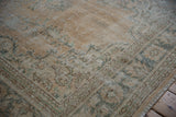 Distressed Oushak rug corner, showing visible wear to knot heads and faded sandalwood, sage patterns.