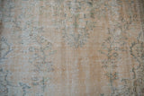Faded floral blossoms, pale green vinery on distressed Oushak carpet pile, foundation visible.
