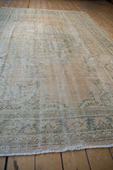 Distressed Oushak rug with mostly even wear, visible foundation, faded green floral pattern, and fringe.