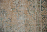Close-up of vintage distressed Oushak rug showing worn sandalwood pile, visible foundation, green vinery.