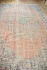 Distressed dusty blush Oushak carpet showing faded royal blue and mint green floral patterns.