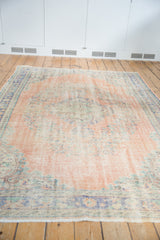 Distressed vintage Oushak carpet with mostly even wear, faded blush, melon, and blue floral patterns.