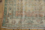 Distressed Oushak rug corner: worn ivory pile, foundation showing, pale mint green border.