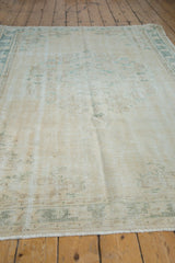 Vintage Distressed Oushak carpet's mostly even wear, highlighting faded ivory and pale teal floral motifs.