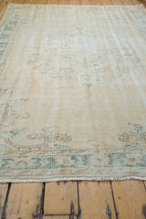 Distressed vintage Oushak carpet's worn ivory pile, pale teal border pattern, and short fringe.